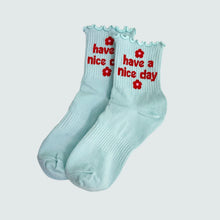 Load image into Gallery viewer, Light blue socks with red text and flower designs on a light gray background